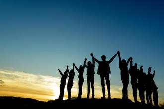 a group of people holding hands in the air standing against a sunset