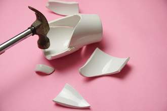 a hammer being lifted after crashing down and breaking a ceramic mug to pieces