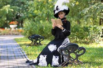a lading in mid-century attire sitting on a park bench reading a book