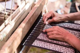 a lady using the loom to make a beautiful piece of fabric