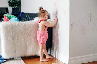 a little girl casually using a red marker to draw on the walls of her home