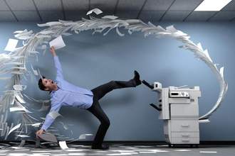 a man bent over backwards while the copy machine in his office shoots out paper chaotically at him