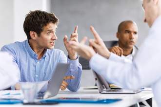 a man defending himself during a meeting while a coworker points at him accusingly