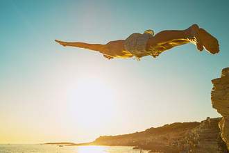 a man dives head-first off a cliff into the ocean