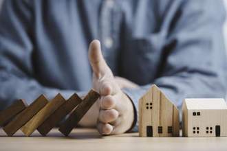 a mans hand blocking a stack of falling blocks from hitting two homes
