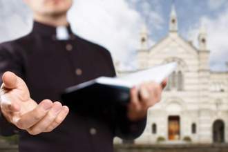 a minister holding out his hand with the other hand holding a bible and a church in the background