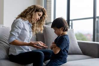 a mother speaking openly to her son who looks upset with his arms crossed firmly