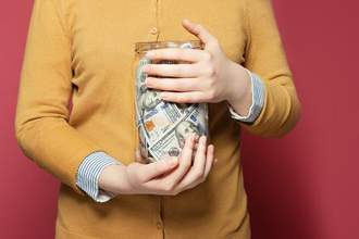 a person holding tightly onto a jar of money