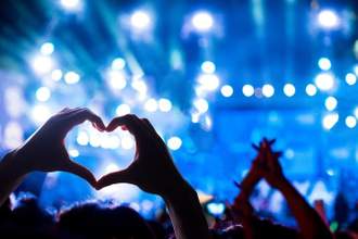 a person holding up their hands in the shape of a heart towards the musician on stage