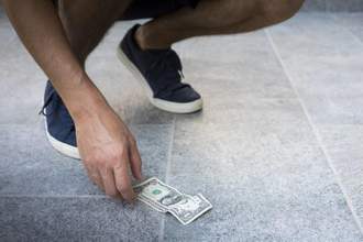 a person reaching down after finding a dollar bill on the ground