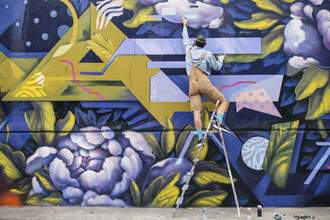 a person standing on a ladder painting a large wall mural