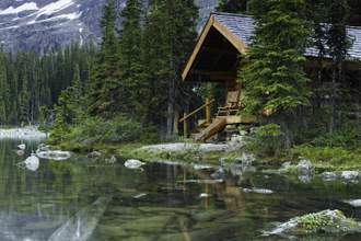 a picturesque view of a cabin in the woods sitting right alongside a clear lake amongst the trees