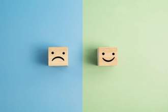 a sad face block sitting on a blue background and a happy face block sitting on a green background