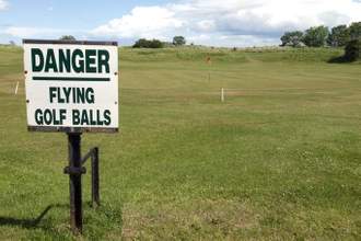 a sign saying danger flying golf balls posted on a golf course