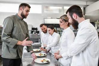 a top chef talking to a junior chef about the food she made while the rest of the class looks on