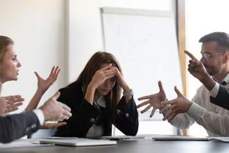 a woman in the office holding her head while her coworkers are yelling at her
