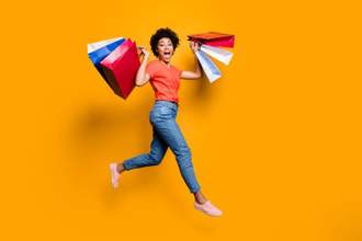 a woman jumping in the air with a handful of shopping bags in front of a yellow backdrop