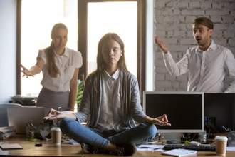 a woman meditating while her coworkers are panicked and chaos is happening in the workplace