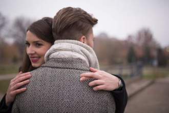 a woman smiling while hugging her significant other with her fingers crossed behind his back