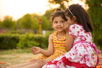 a young girl whispers in her friends ear