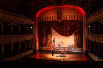 a zoomed out view of the theatrical stage with beautiful set design and actors in their respective spots rehearsing