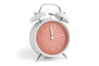 alarm clock with pink face sitting on white background