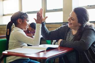 an excited teacher giving one of her students a high five while in class