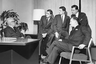 an old photograph of a group of businessmen listening to their boss