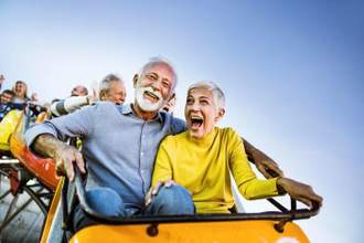 an older lady and gentleman sitting front row on a roller coaster screaming and enjoying the ride