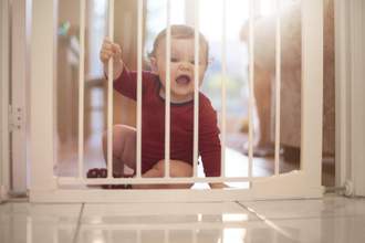 baby sitting on the ground beside a baby gate yelling to get the attention of parents