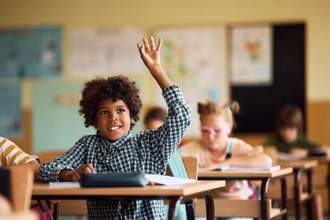 boy sitting at his desk in class raising his hand