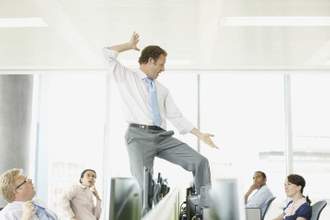 business man dancing on top of a table while his coworkers look on in shock