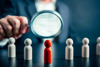 business man holding a magnifying glass up to a uniquely colored peg