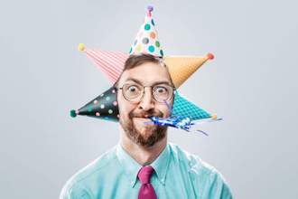 business man with five birthday hats on his head blowing on a party horn blower