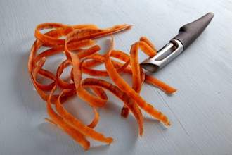 carrot peelings and black metal peeler on a light wooden table