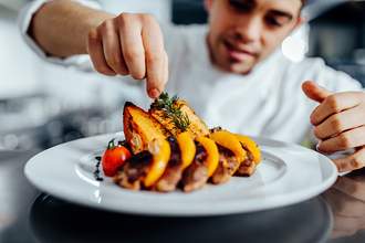 chef putting green sprig on plate of food