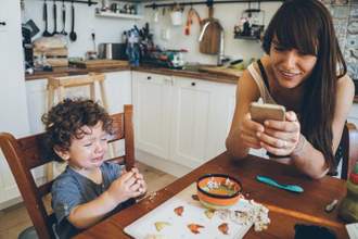 child crying while eating and their mother is on their phone not paying attention