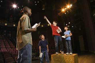 child standing on soapbox rehearsing lines while three other children look up at him in amazement