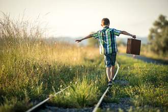 child with suitcase walking on old railroad tracks