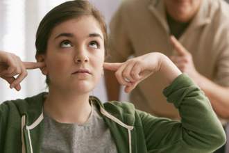 daughter with fingers in her ears while father scolds her