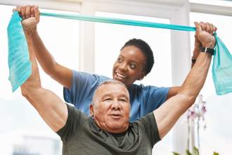 doctor helping a senior with arm band stretches during physical therapy