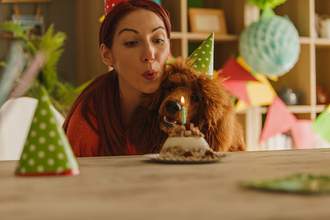 dog and human in party hats blowing out candles on a cake