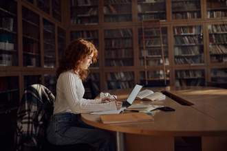 female student taking notes on her computer while in library