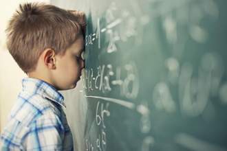 frustrated kid leaning head first against a chalk board