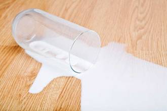 glass tipped over with milk spilled out on a wooden table