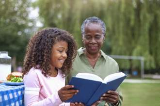 granddaughter reading book with grandmother at public park picnic