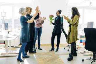 group of women standing around their coworker applauding her