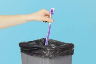 hand getting ready to throw an old toothbrush into a trash can