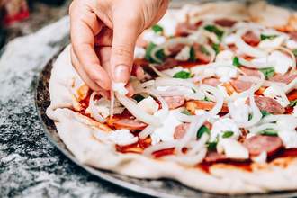 hand placing topping on pizza