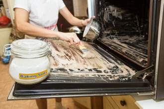 hands scrubbing hot water and baking soda in their oven to remove grease stains